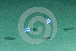 Two blue dices falling on a green table