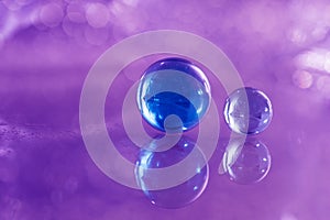 Two blue glass balls on a glass table. Glass balls on a purple background with reflection.