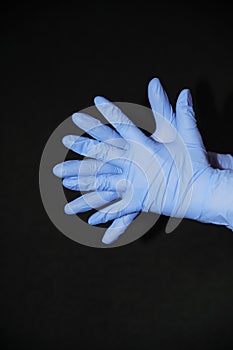 Two blue gloved hands, palms against palm, fingers offset, on black background