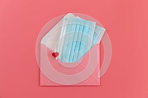 Two blue medical face masks and pink envelope fastened with a clothespin with a heart on pink background.