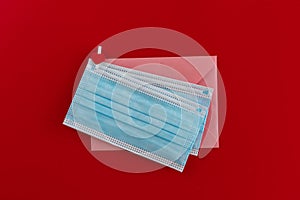 Two blue medical face masks and pink envelope fastened with a clothespin with a heart on red background.