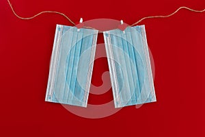 Two blue medical masks are hung on clothespins with hearts on a string on a red background.