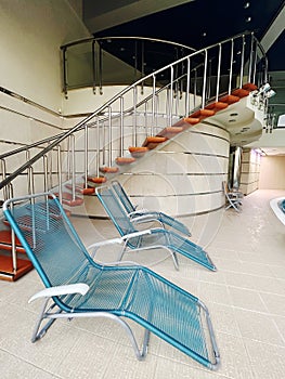 Two blue outdoor sunloungers by a spiral staircase in the building