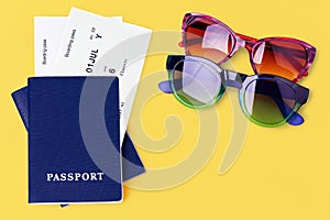 Two blue passports, boarding pass, flight ticket, sunglasses on yellow background, airplane travel, summer holidays, vacation