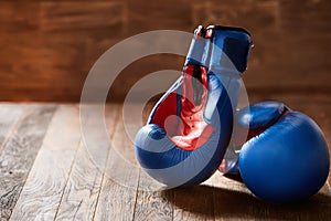 Two blue and red boxing gloves on brown wooden plank against wooden background.