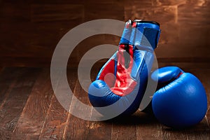 Two blue and red boxing gloves on brown wooden plank against wooden background.