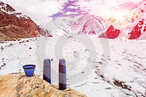 Two Blue travel thermoses Thermo Bottles and Cup on stone and Base Camp in High Mountains