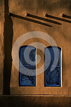 Two Blue WIndows and long shadows against warm Adobe Walls in downton Santa Fe New Mexico