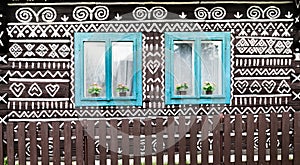 Two blue wooden windows on the White and black pattern ornament painting on the dark wood wall in Slovakian old village Cicmany.