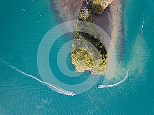 Two boats go around a rocky island in a tropical sea