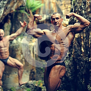 Two bodybuilders posing in a cave