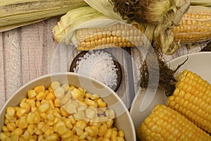 Two boiled ears of corn, corn kernels, coarse salt and raw ears of corn on a wooden table. Fitness diet. Healthy diet. For a sweet