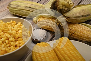 Two boiled ears of corn, corn kernels, coarse salt and raw ears of corn on a wooden table. Fitness diet. Healthy diet. For a sweet