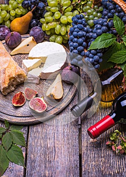 Two bottle of red and white wine, grapes, cheese, cork, corkscrew, white bread on a dark background