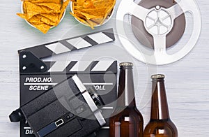 two bottles of beer, a bucket of nachos, a movie clapper with an old video camera and a film strip