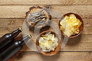 Two Bottles of beer with chips and dried smelt fish on  wooden background dark stone background