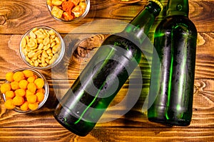 Two bottles of beer and different snacks on wooden table. Top view