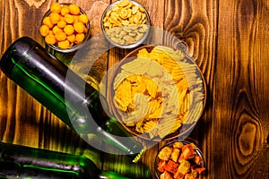 Two bottles of beer and different snacks on wooden table. Top view