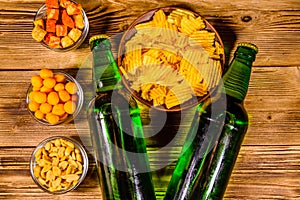 Two bottles of beer and different snacks on wooden table. Top view