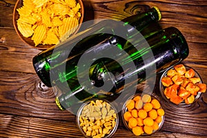 Two bottles of beer and different snacks on wooden table. Top view