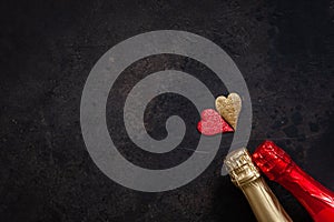 Two bottles of champagne and two hearts simbols. Top view, close-up, flat lay on dark brown background