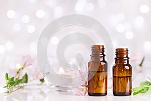 Two bottles with essential oil, flowers and candles on white table with bokeh effect. Spa, aromatherapy, wellness, beauty theme.