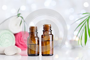 Two bottles with essential oil, towel and candles on white table with bokeh effect. Spa, aromatherapy, wellness, beauty theme.