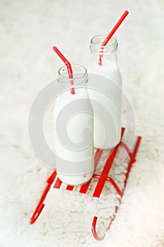 Two bottles of fresh milk with red straws on decorative sleds