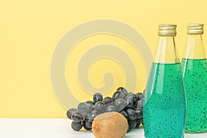Two bottles of fruit cocktail, grapes and kiwis on a yellow background