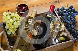 Two bottles, glasses of wine, bunches of grapes in wooden box