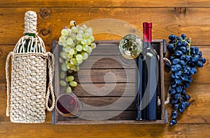 Two bottles with glasses of wine and grapes on a wooden background.