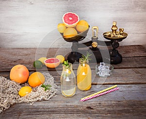 Two bottles with homemade lemonade and orange fresh juice with mint and ice on the rustic wooden background with fresh citrus in