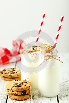 Two bottles of milk with striped straws and cookies on the white wooden background