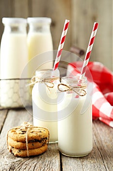 Two bottles of milk with striped straws on the grey wooden background