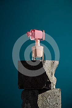Two bottles with pink and beige nail polish on the cement cubes,