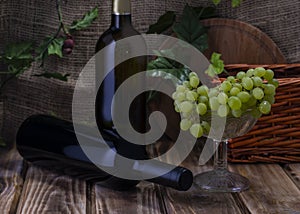 Two bottles of red and white wine on a wooden table with a bunch of grapes