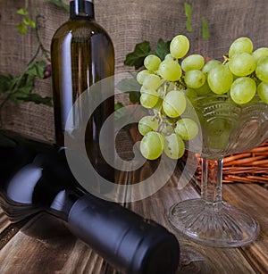 Two bottles of red and white wine on a wooden table with a bunch of grapes