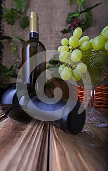 Two bottles of red and white wine on a wooden table with a bunch of grapes