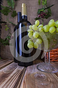 Two bottles of red and white wine on a wooden table with a bunch of grapes