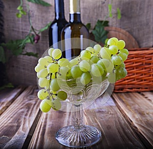 Two bottles of red and white wine on a wooden table with a bunch of grapes