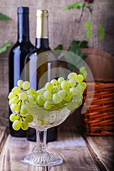 Two bottles of red and white wine on a wooden table with a bunch of grapes