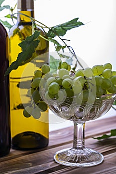 Two bottles of red and white wine on a wooden table with a bunch of grapes