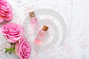 Two bottles with rose oil, crystals of mineral bath salts and pink roses on the wooden table