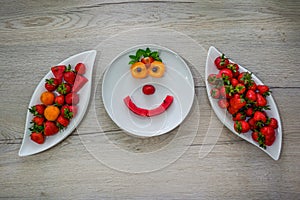two bowl of fresh red strawberries and apricots and water melon on the table and fruit smile