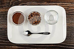 Two bowls with ground coffee and roasted coffee beans, coffee cup, spoon in plate on wooden table. Top view