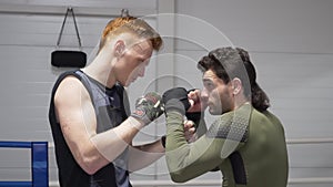 Two boxers in boxing bandage standing in ready pose on boxing ring. Kickboxer fighters posing front camera in fight club