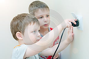 Two boy brothers with interest and curiosity insert the plug into the socket. Dangerous play for children, possible electric shock