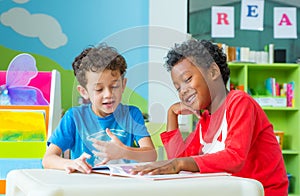 Two boy kid sit on table and reading tale book in preschool lib