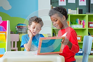 Two boy kid sit on table and reading tale book in preschool lib