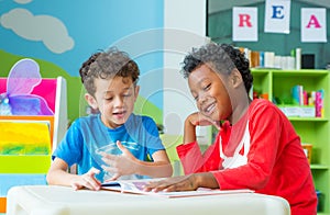 Two boy kid sit on table and reading tale book in preschool lib photo